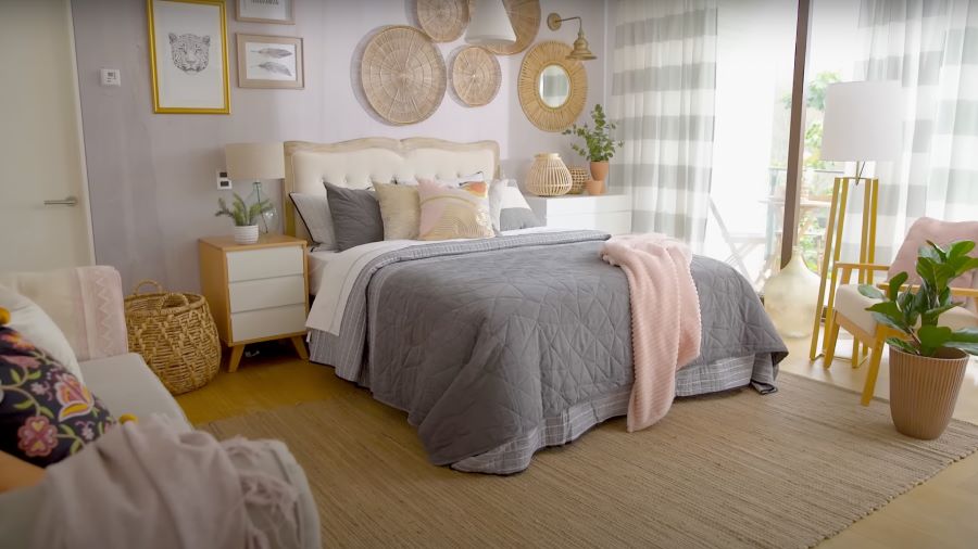 Dormitorio estilo clásico con gran ventanal con cortinas de tela con líneas grises y blancas. Cama con cubrecama gris y manta rosada. Respaldo de cama beige.