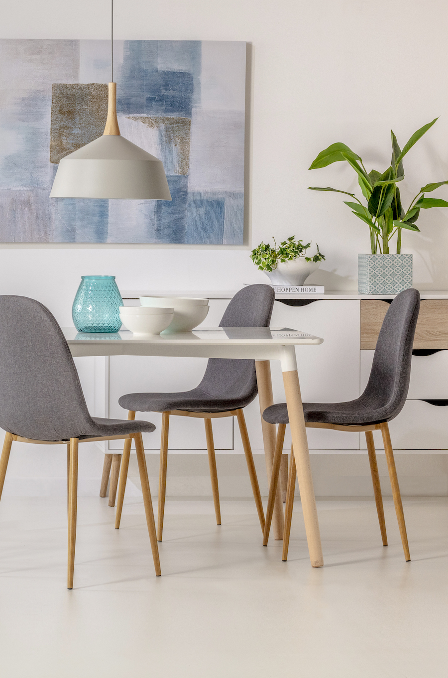 Comedor estilo nórdico moderno con color de piso beige claro. Mesa de comedor con patas de madrea y base blanca, tres sillas grises estilo eames.