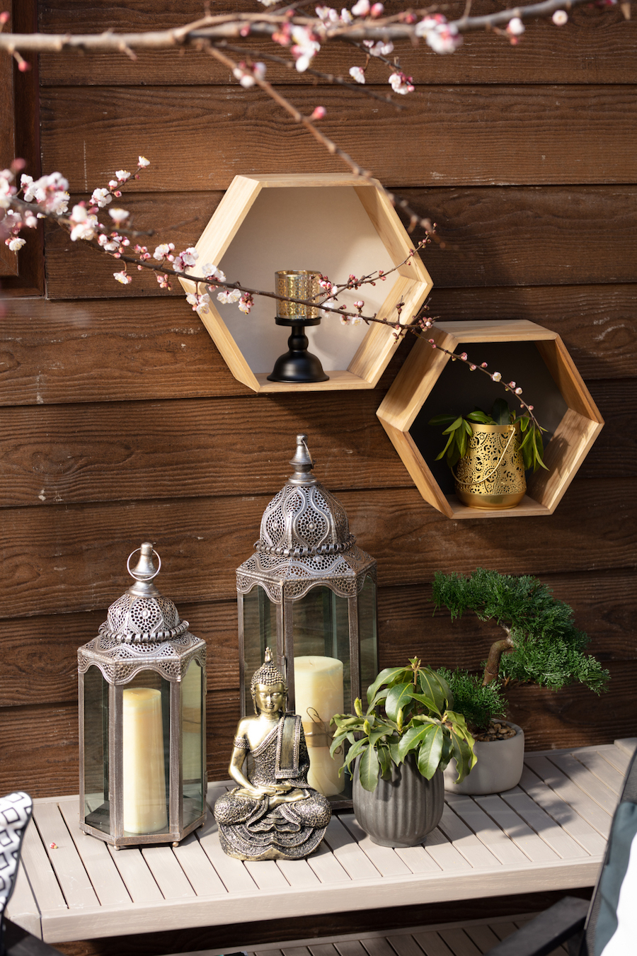 Detalle de terraza de invierno con decoraciones estilo zen. Fanales metálicos y vidrio con velas, imagen de buda y plantas en maceteros. Dos repisas hexagonales en la pared