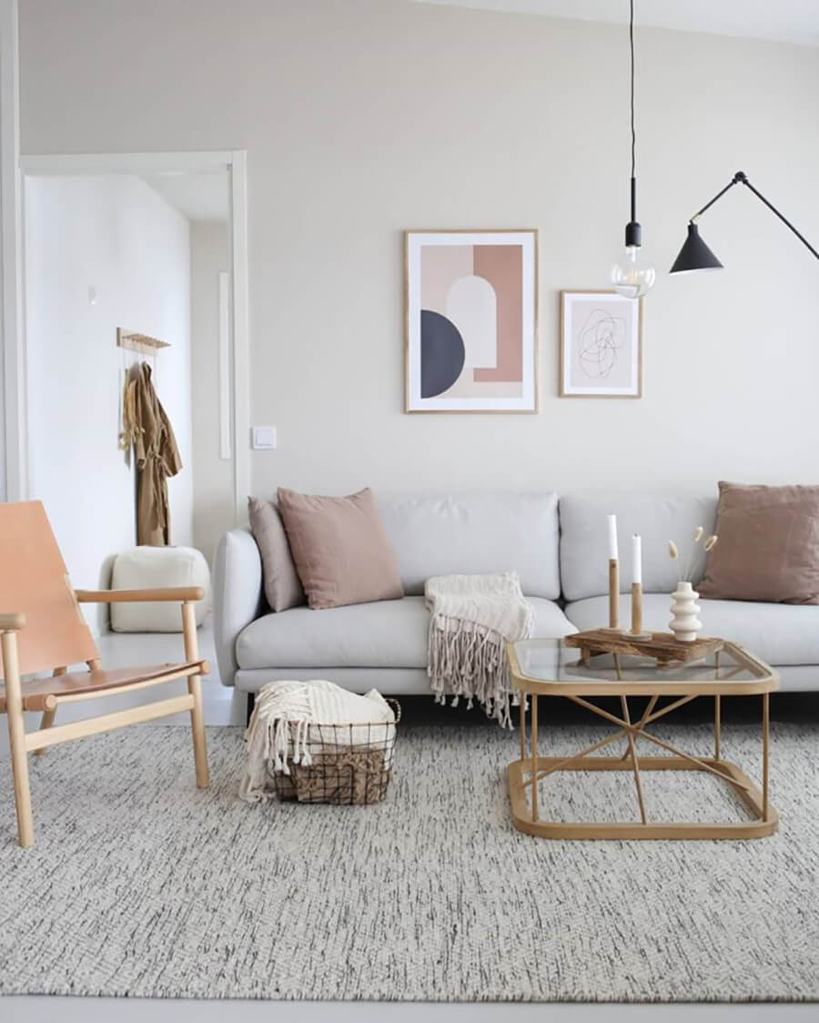 Living con decoración nórdica. Alfombra en tonos grises, paleta de colores claras. Acentos de colores en cojines decorativos, arte y silla. 