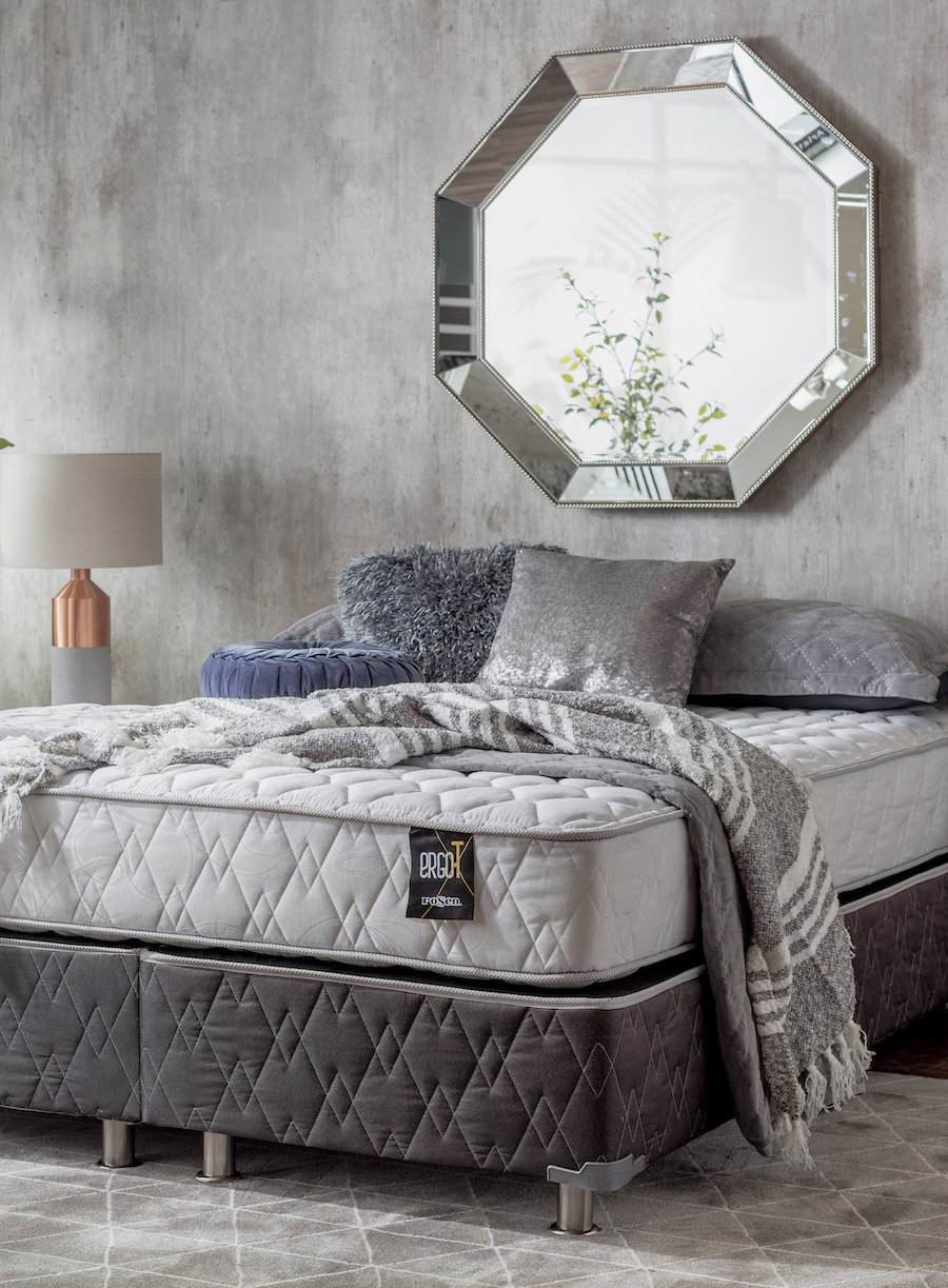 Dormitorio de estilo Ejecutivo urbano con una pared de concreto gris que sostiene un gran espejo hexagonal de marco biselado sobre el cabecero de la cama. 