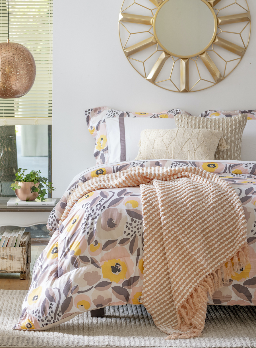 Espejo de marco dorado con diseño vintage sobre el respaldo de una cama con cobertor de colores amarillas y lilas. 