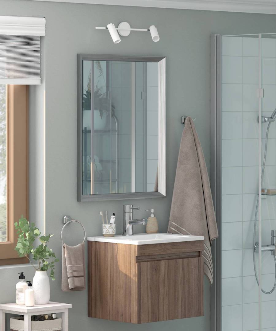 Baño de estilo nórdico con un vanitorio de madera y un espejo anti-empañante con marco plateado junto a una ducha con cerámicos blancos y grifería gris.
