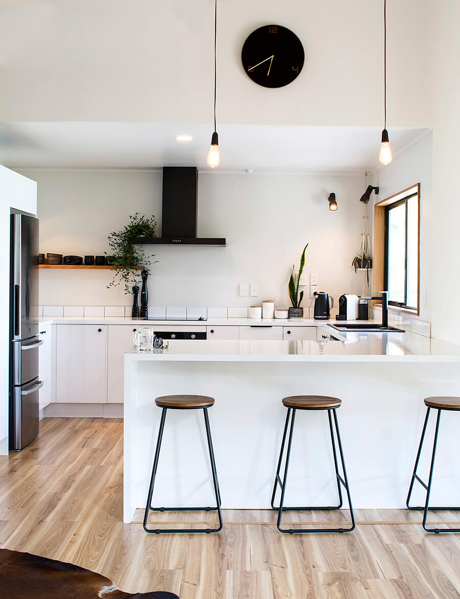 Una cocina abierta con un mesón blanco que delimita el espacio y pisos altos negros con asiento de madera