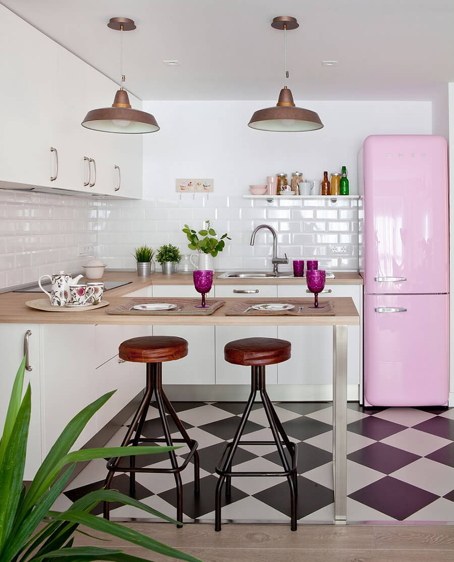 Una cocina abierta con un mesón de madera y un refrigerador rosado pastel y piso de cerámicas ajedrez