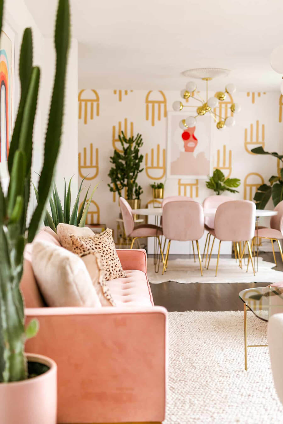 un living comedor con un sofá color rosa pastel y sillas de comedor de color rosa, con plantas como decoración