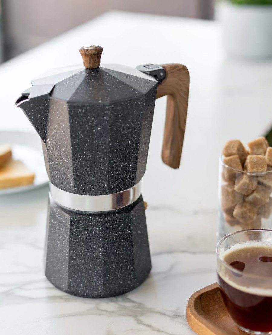 Primer plano de una cafetera italiana color negro. Junto a ella hay una taza de café y un recipiente transparente con cubos de azúcar rubia.