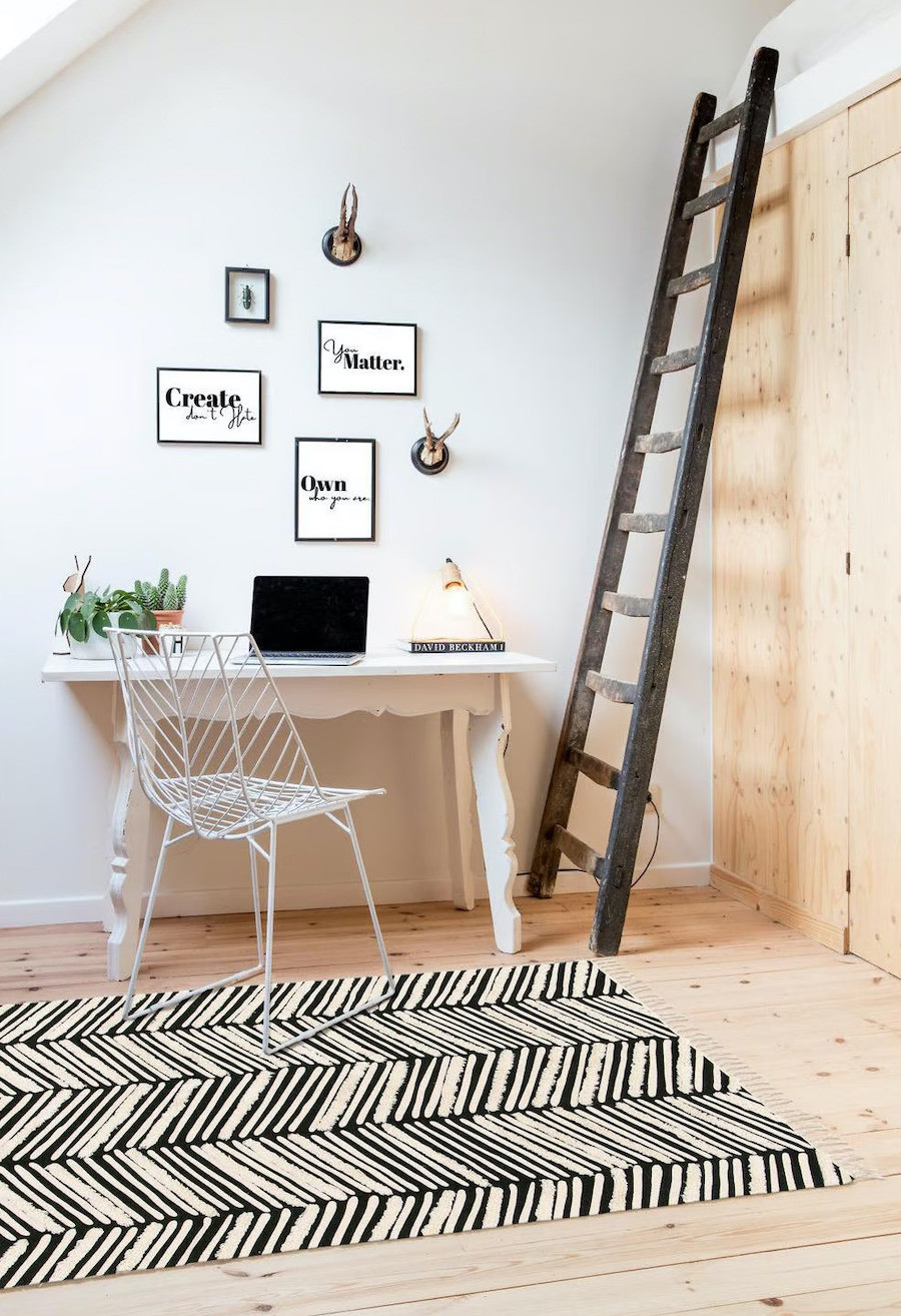 Sala de estar con mesa blanca y silla metálica. Closet de madera con gran escalera negra apoyada en la pared. Alfombra con diseño zigzag en blanco y negro