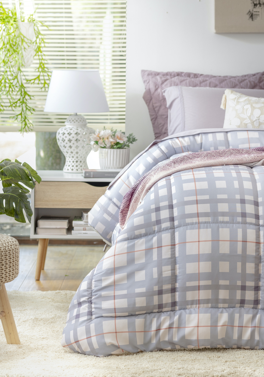 Dormitorio estilo clásico, cama con plumón estampado cuadrillé, de color blanco, celeste y líneas rojas. Velador nórdico con lámpara blanca y flores