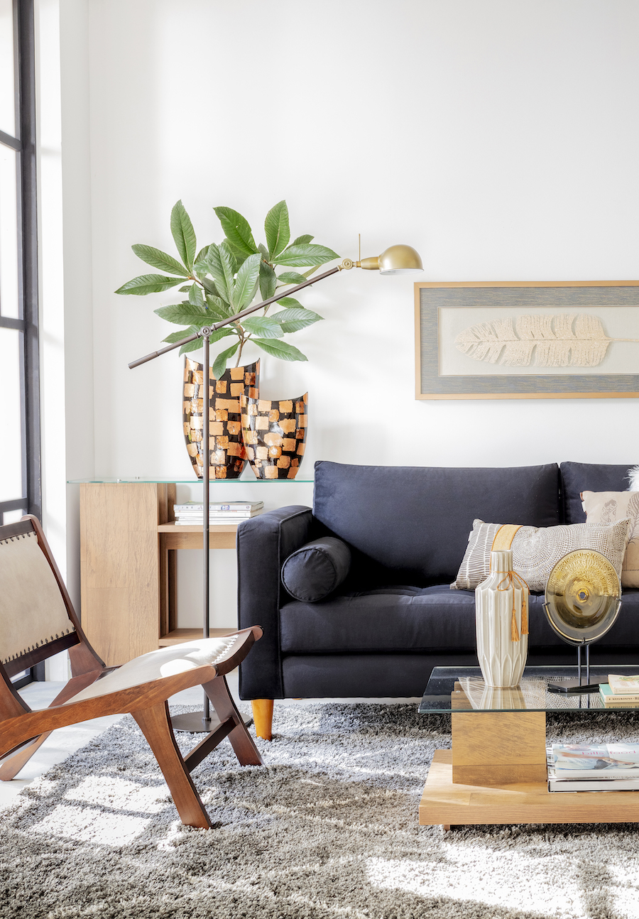 Living de estilo moderno con sofá de dos cuerpos azul marino, de líneas simples y look minimalista. Poltrona de madera y ratán, mesa de centro de vidrio y base de piedra,