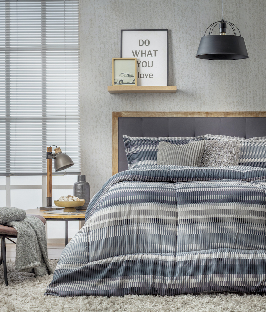 Dormitorio estilo clásico industrial. Cama de dos plazas con plumón de líneas color azul, gris y blanco. Respaldo de cama gris con marco de madera.