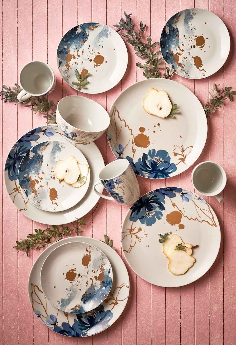Toma de una mesa rosada de madera con vajilla blanca con diseño de flores y hojas azul marino y café claro.
