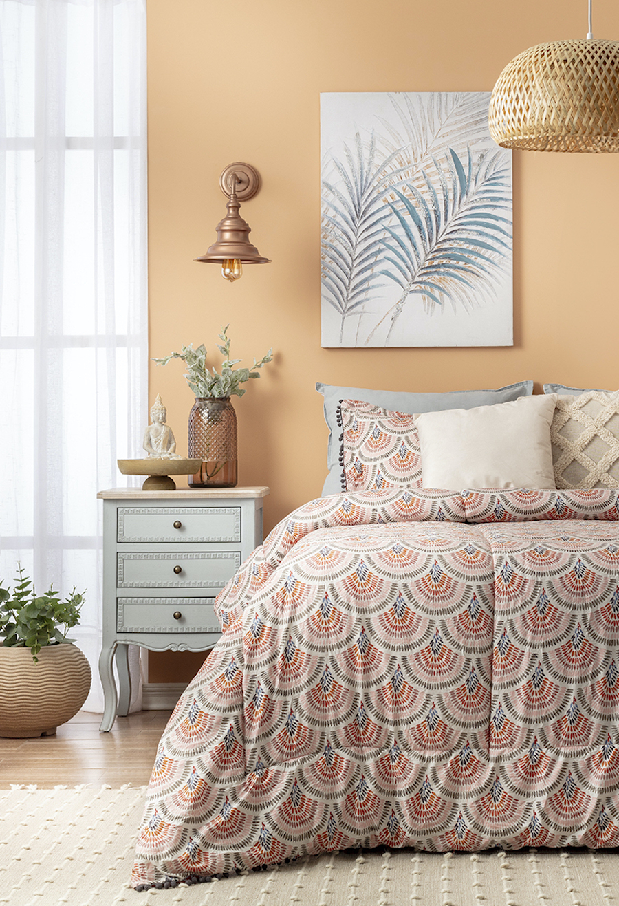 Dormitorio de estilo Boho chic y paredes color salmón, cama con plumón de diseño en tonos rojizos y grises, cojines en tonos arena y un velador celeste pastel con adornos boho.