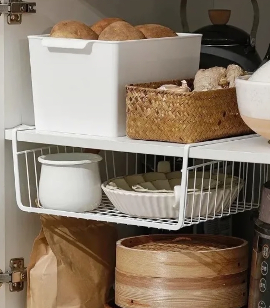 Detalle de un mueble de cocina abierto con canastos plásticos y de mimbre como organizadores. Bandeja plástica bajo uno de los estantes