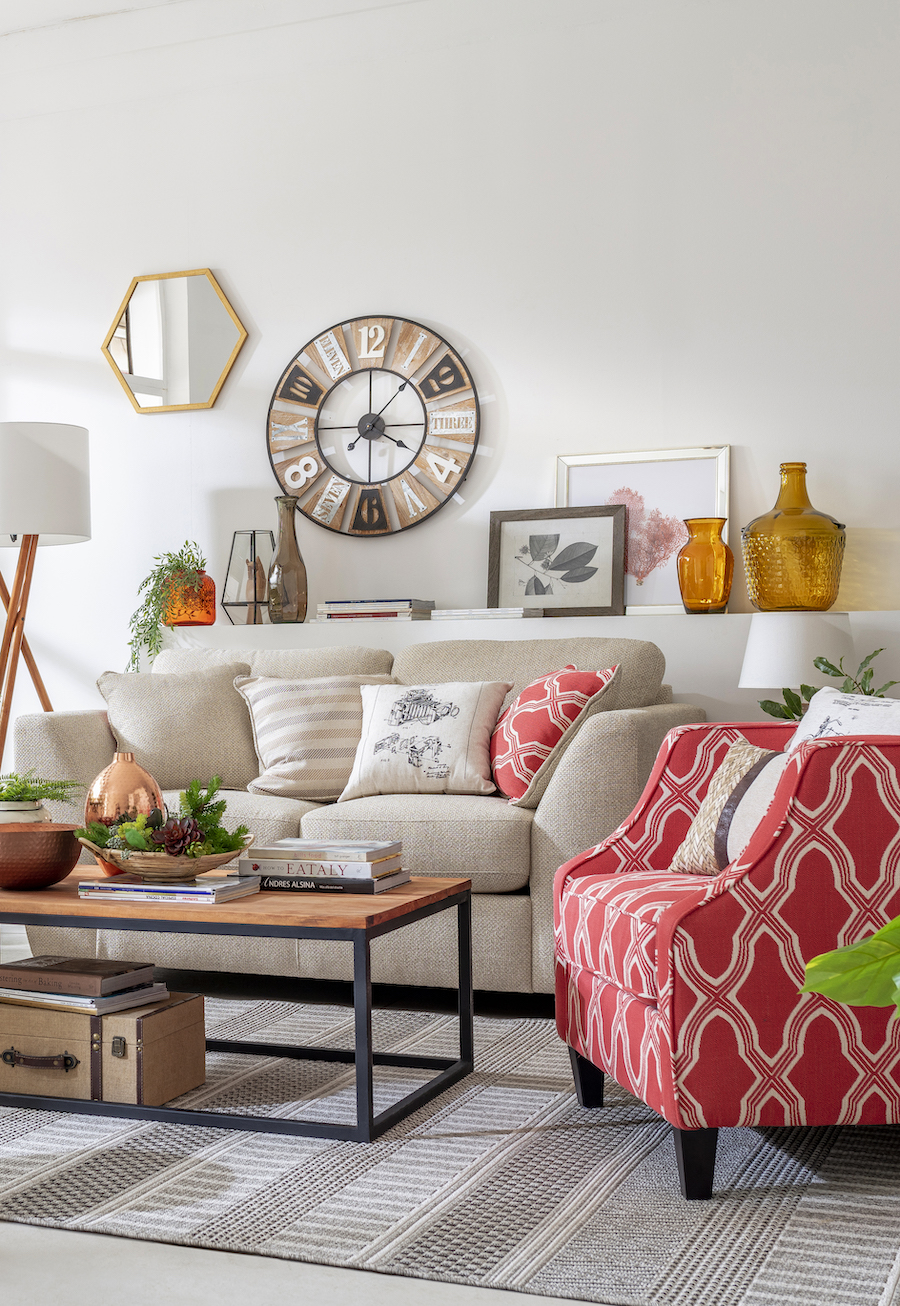 Living con la teoría del rojo inesperado. Sofá beige junto a una poltrona con tapiz rojo con blanco. Mesa de centro de madera y patas de metal negro.