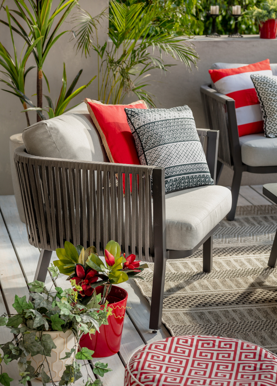 Muebles de terraza con la teoría del color rojo inesperado. Sitial negro con cojines gris claro, gris oscuro y rojo. 