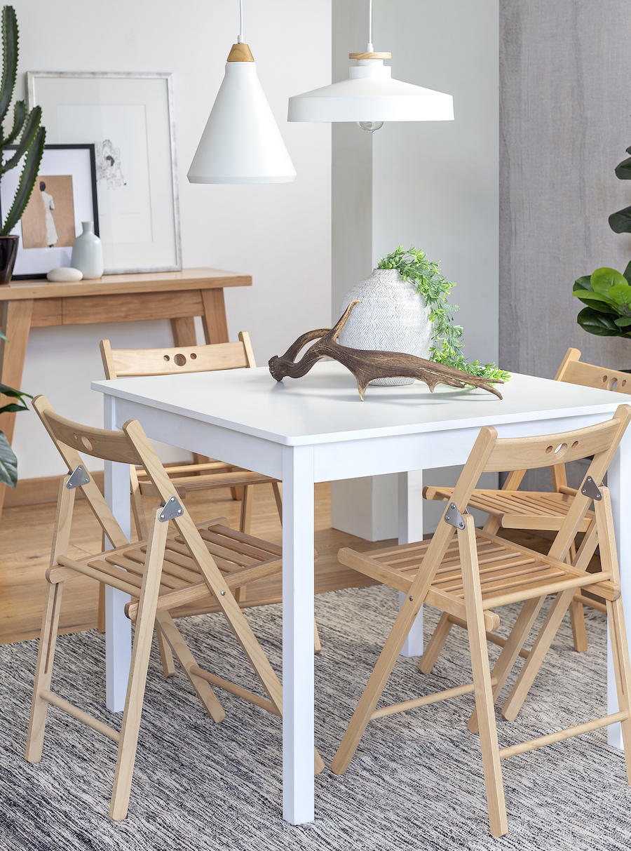 Comedor pequeño de estilo nórdico con una mesa blanca rectangular y 4 sillas de madera plegables.