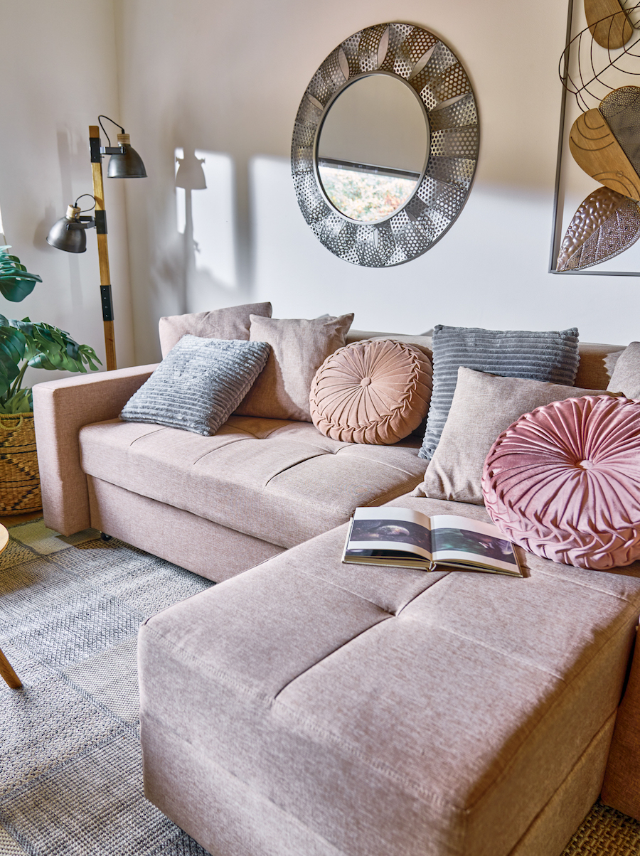 Sala de estar de tonos neutros con un futón seccional beige con cojines grises, beige, rosado y anaranjado pastel. 