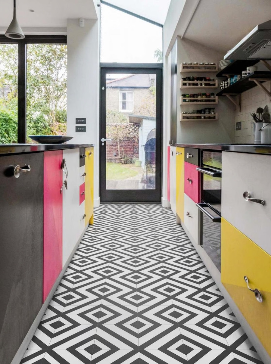 Gran cocina iluminada con pisos con cerámicos geométricos. Muebles de cocina de colores negro, blanco, rosado y amarillo.