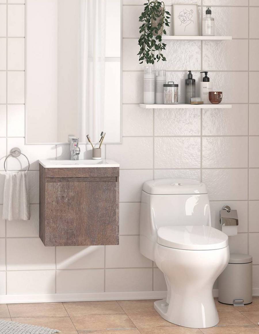 Baño de cerámicas de muro blancas, WC blanco y mueble vanitorio flotante de madera y lavamanos blanco. Sobre él hay un espejo rectangular y sobre el inodoro, una repisa flotante blanca con diferentes artículos de higiene.