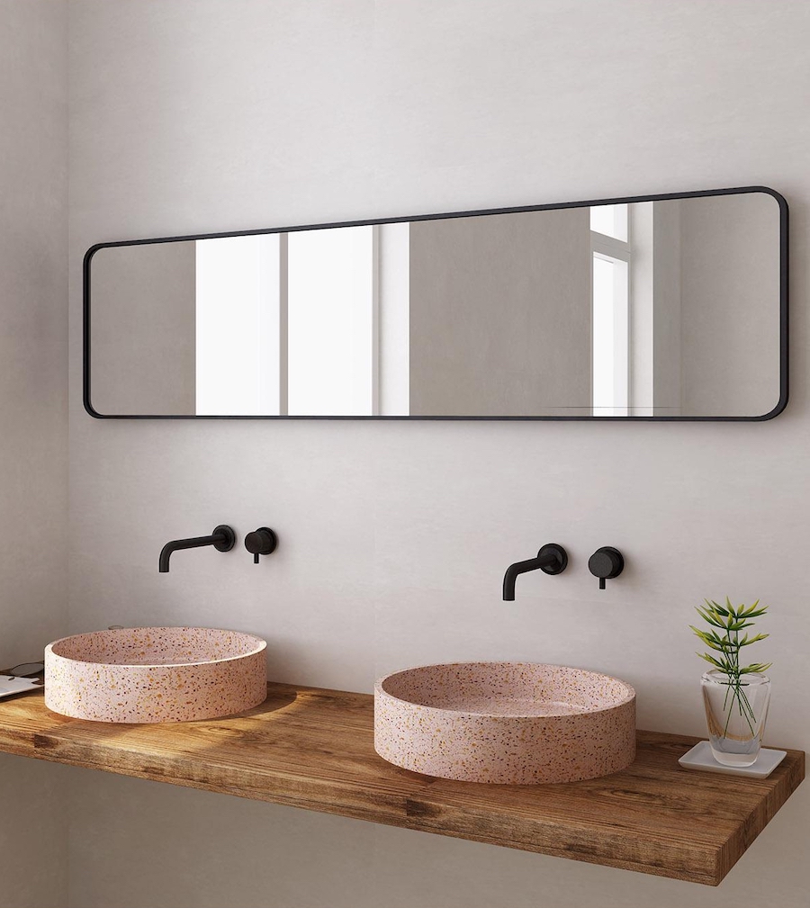 Baño rústico moderno con vanitorio de madera y dos lavamanos de cerámica rosa, redondos. Grifería negra empotrada y gran espejo rectangular con marco negro