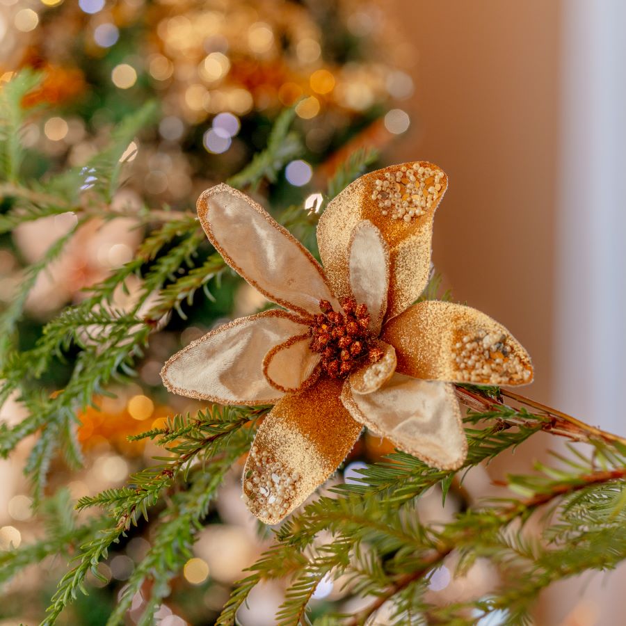 Detalle de flor de tela para decorar el árbol de Navidad. Es dorada con pequeñas semillas rojas al centro.