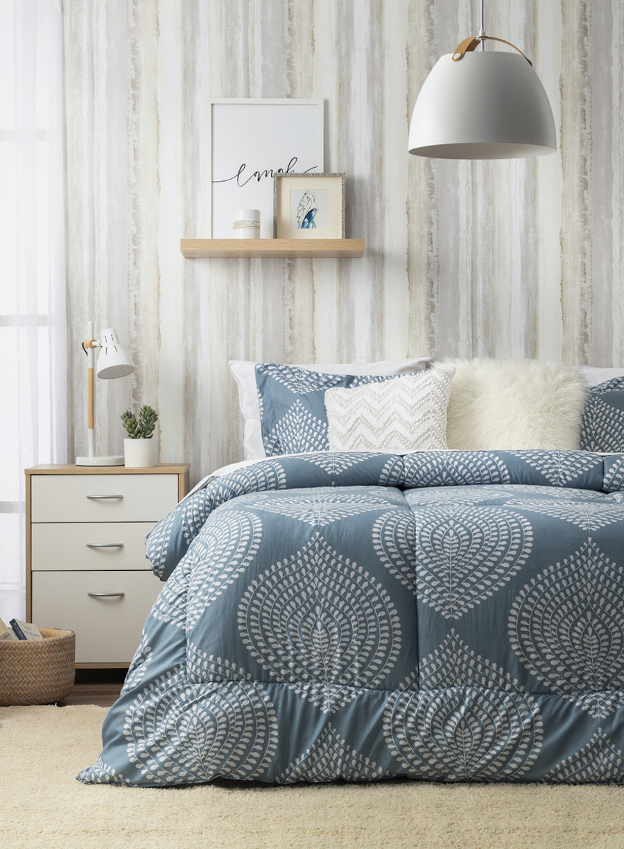 Dormitorio de estilo nórdico con una pared con papel mural que simula ser madera gris, una cama con un plumón azul con diseño de hojas blancas.