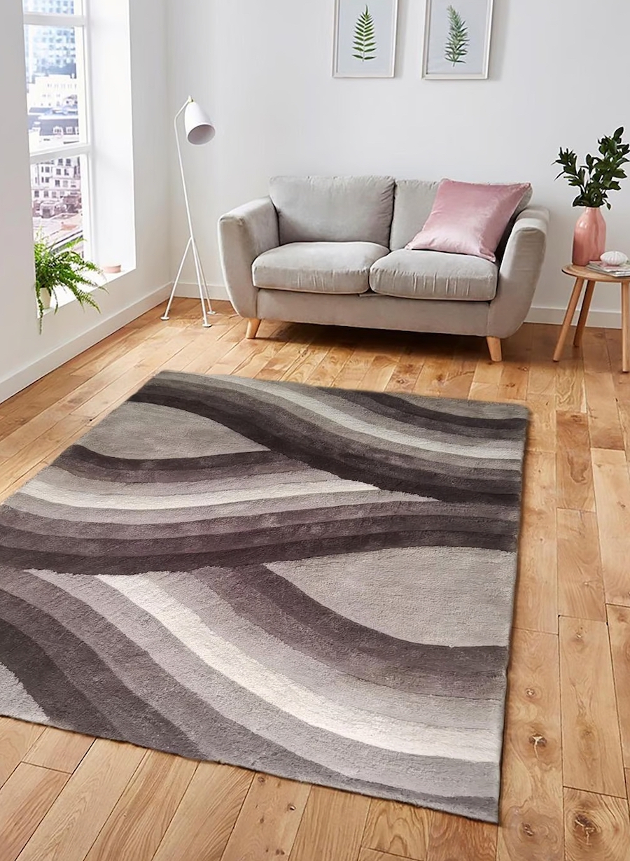 Living moderno con gran alfombra al centro con líneas curvas en tonos negro, gris y blanco. Atrás se ve un pequeño sillón nórdico gris