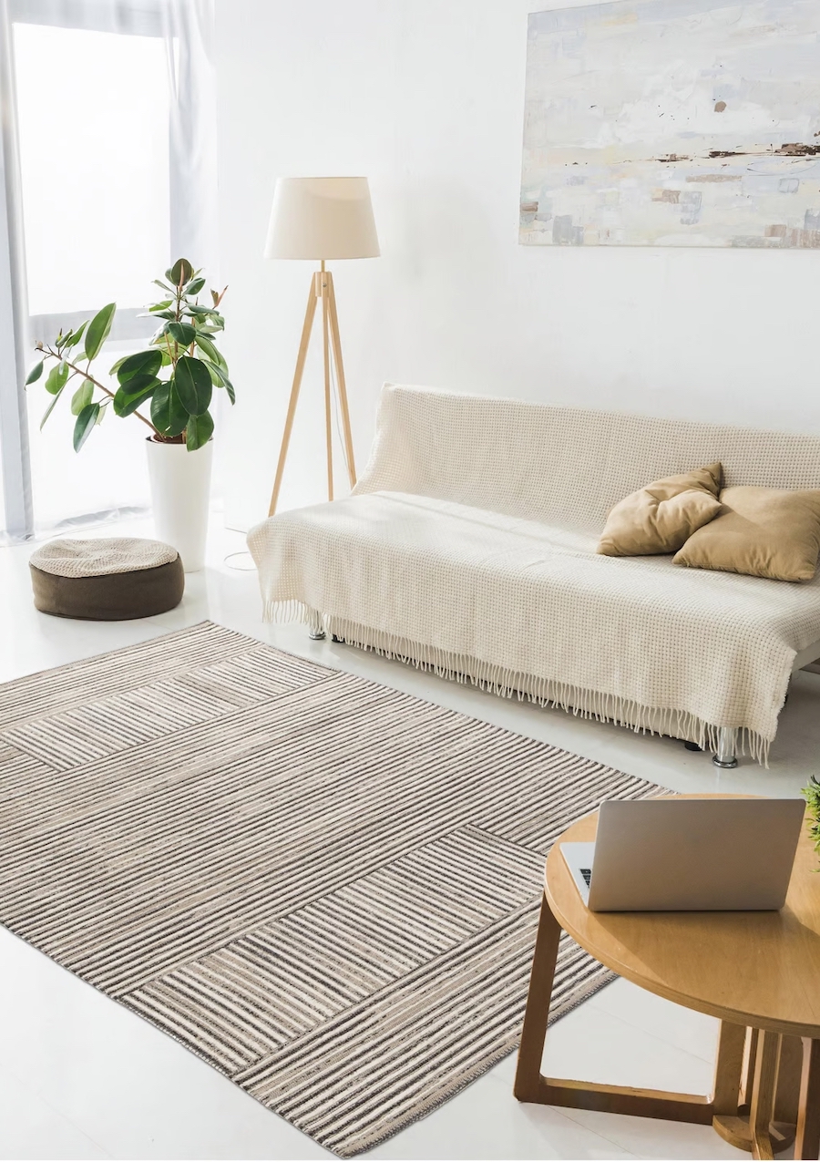 Living moderno, muy luminoso con alfombra al centro en tonos beige y negro. Sillón con manta beige y lámpara de pie de madera.