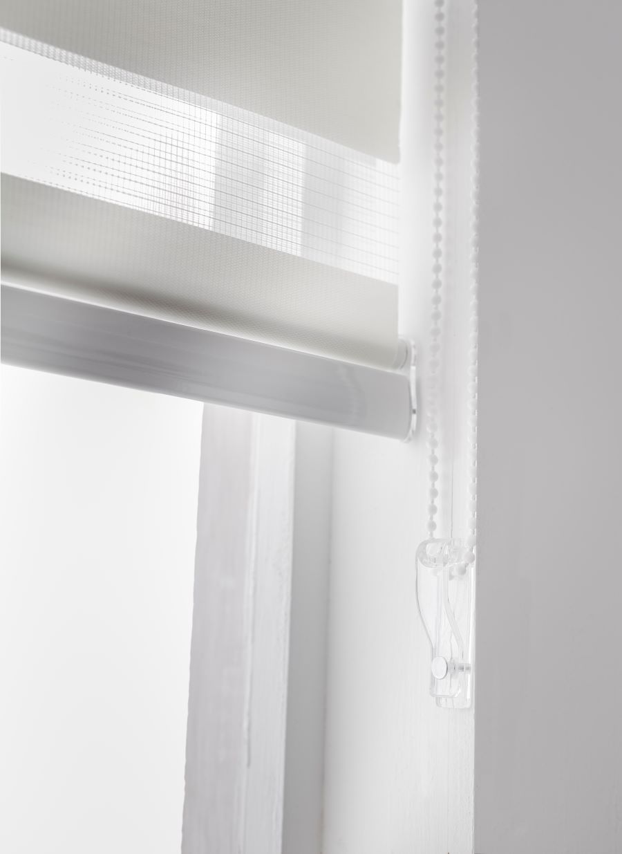 Detalle de cortina roller duo blanca con tiradores transparentes. Muros blancos