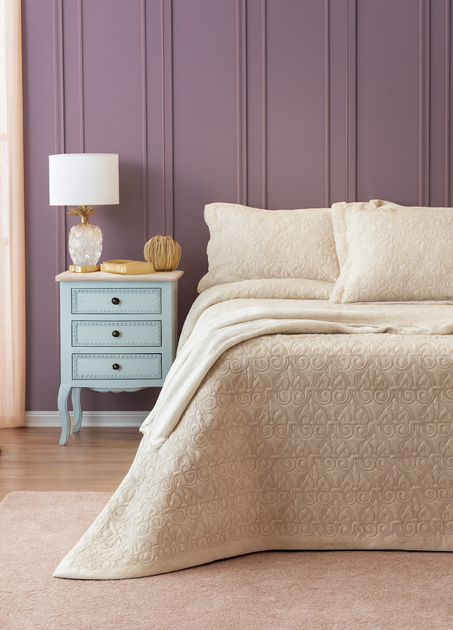 Dormitorio con muros en lavanda suave, ropa de cama beige y detalles decorativos en celeste y dorado, creando un ambiente sereno y contemporáneo.