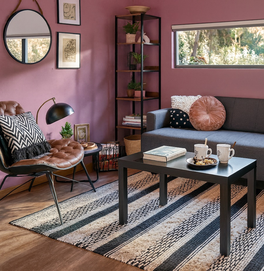 Living acogedor con muro en tono rosado oscuro, sofá gris y accesorios negros, perfecto para un ambiente relajado y actual.