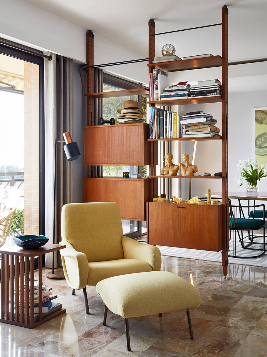 Decoración vintage moderno de living comedor, con sillón o poltrona en tonos mostaza y reposapiés a juego, muebles de madera de diseños sencillos y comedor al fondo