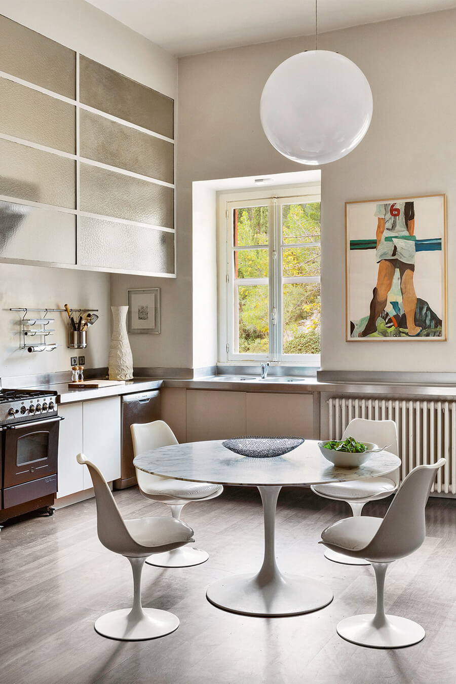 Cocina abierta con comedor de mesa redonda y sillas blancas con formas curvas. Los muebles de cocina, el suelo y las paredes son de colores neutros.