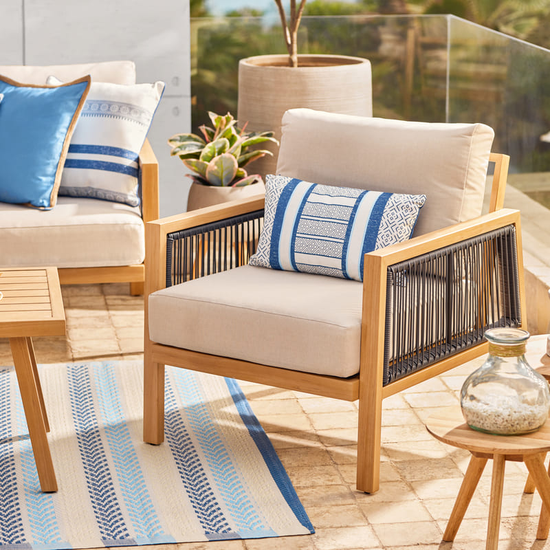 Juego de terraza color crema con marcos de madera, cojines y alfombras con detalles azul y celeste.