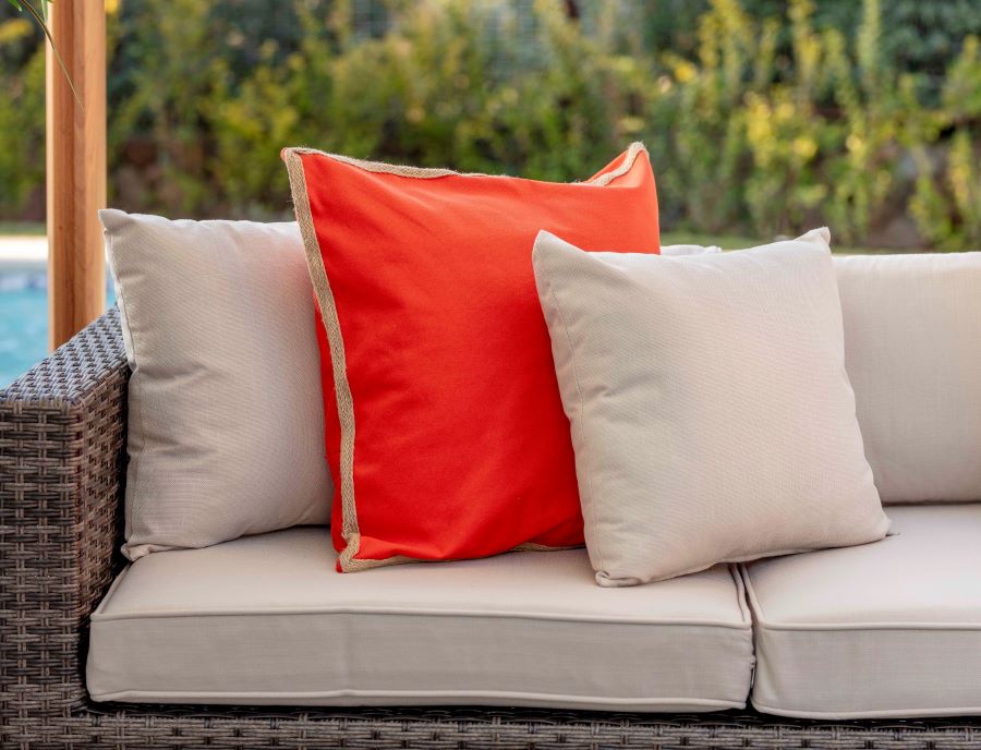 Detalle de sofá de terraza con cojines beige y un cojín naranjo