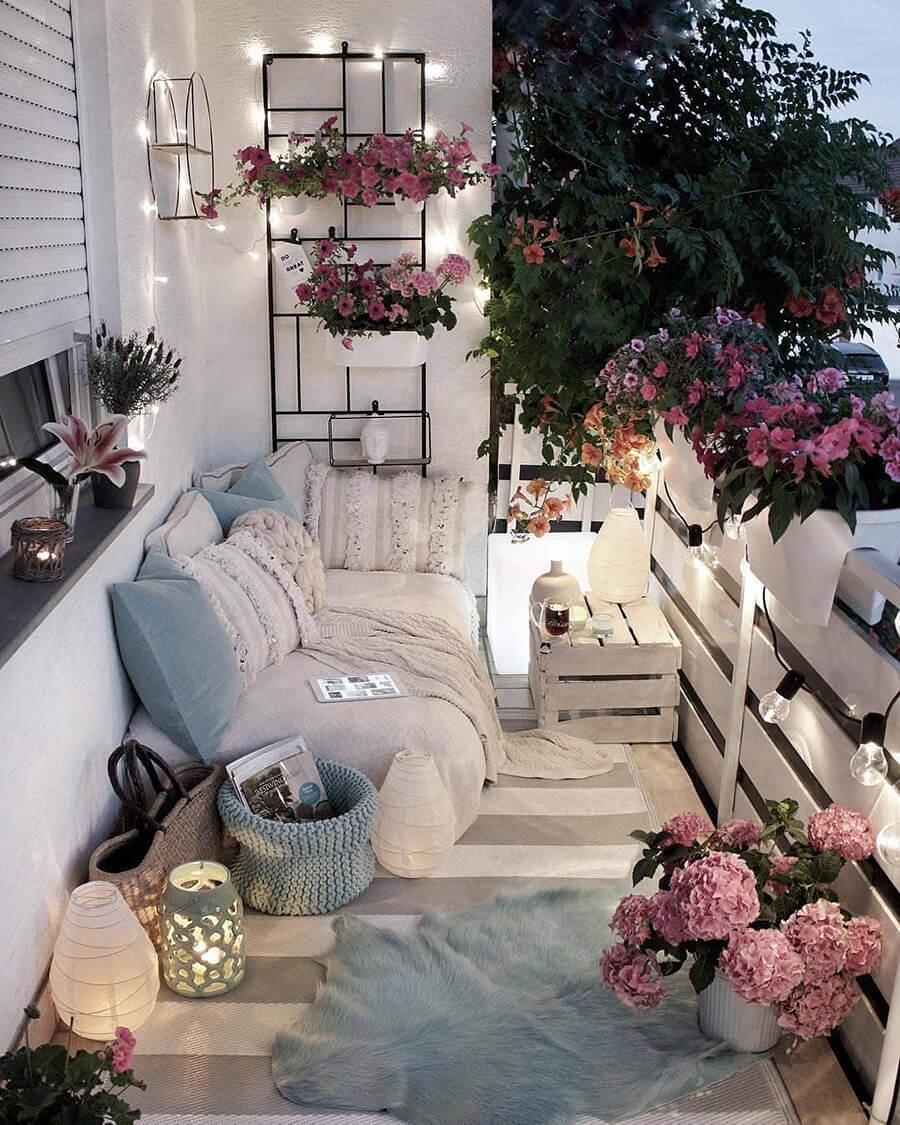 Terraza con varios textiles decorativos y decoración en tonos neutros, con flores en tonos rosados. Un sofá con cojines, mantas y dos alfombras.