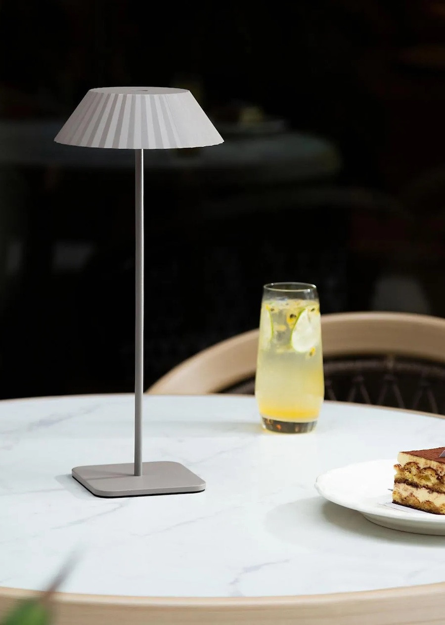 Detalle de una mesa de exterior con una lámpara led inalámbrica, un vaso de jugo y un pastel.