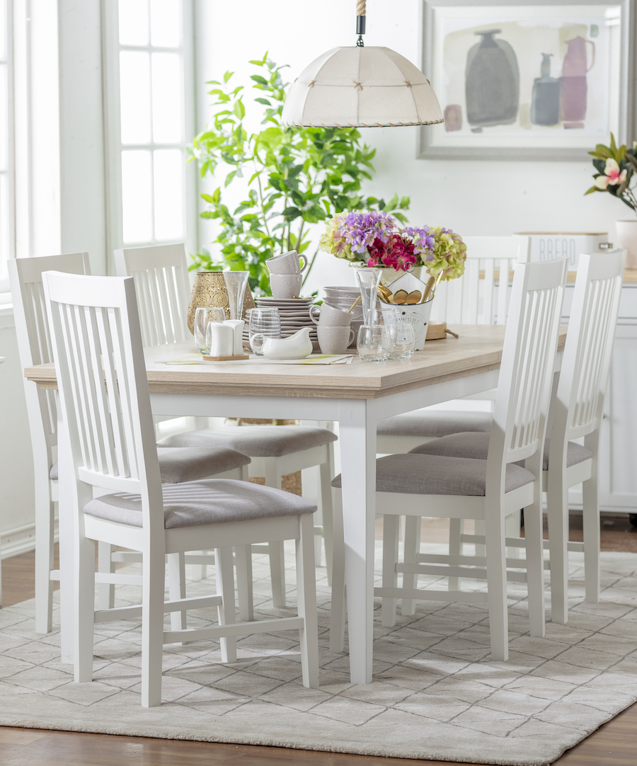 Comedor de muros, alfombra, mesa y sillas blancas. Sobre la mesa hay menaje en tonos blancos y grises, flores de colores y otras decoraciones.