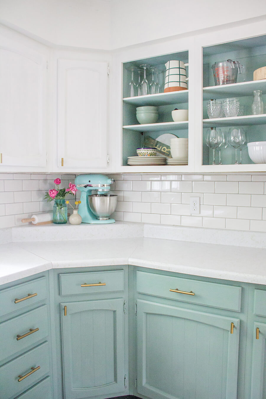 Una cocina de color blanco en que el mueble y el fondo de las vitrinas están pintados del mismo color turquesa pastel.