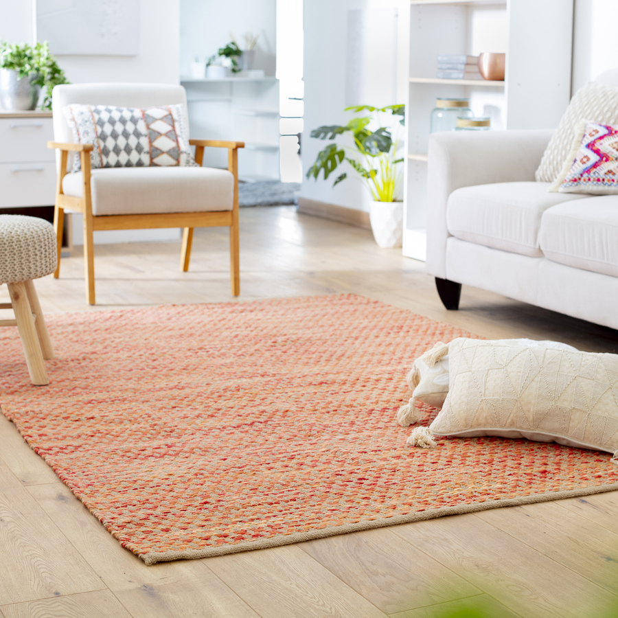 Living clásico con gran alfombra café y roja. Sobre ella hay dos cojines, un piso, un sitial de madera y tela beige y un sillón blanco de tres cuerpos.